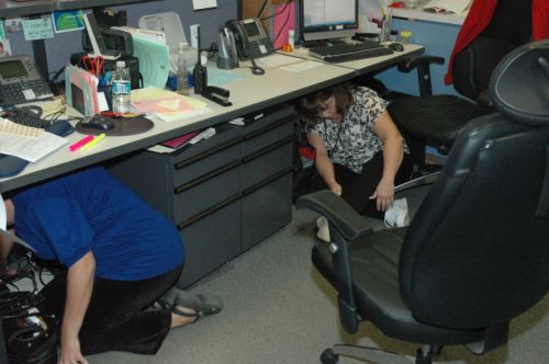 2 female staff ducking under office desk during drill